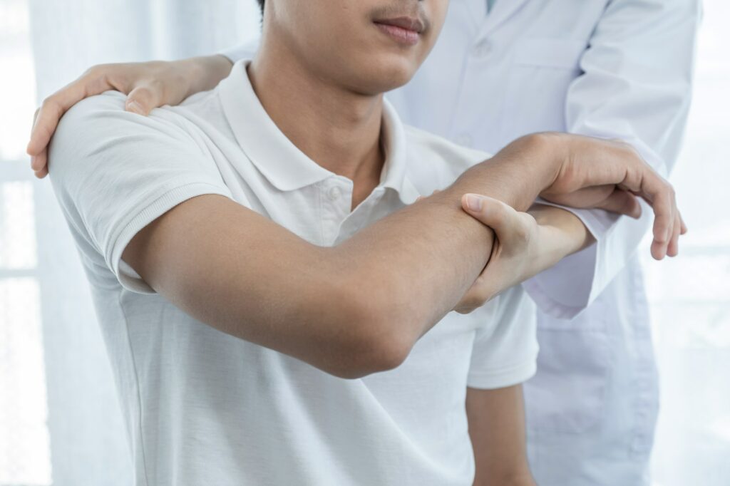 Woman doctor doing physical therapy By extending the shoulder of a male patient